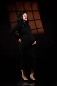 Elegant maternity photoshoot of a pregnant woman in black dress with warm studio lighting by Secret Vows Photography